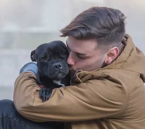 Gentleman is sitting on the ground hugging and kissing his black puppy lovingly