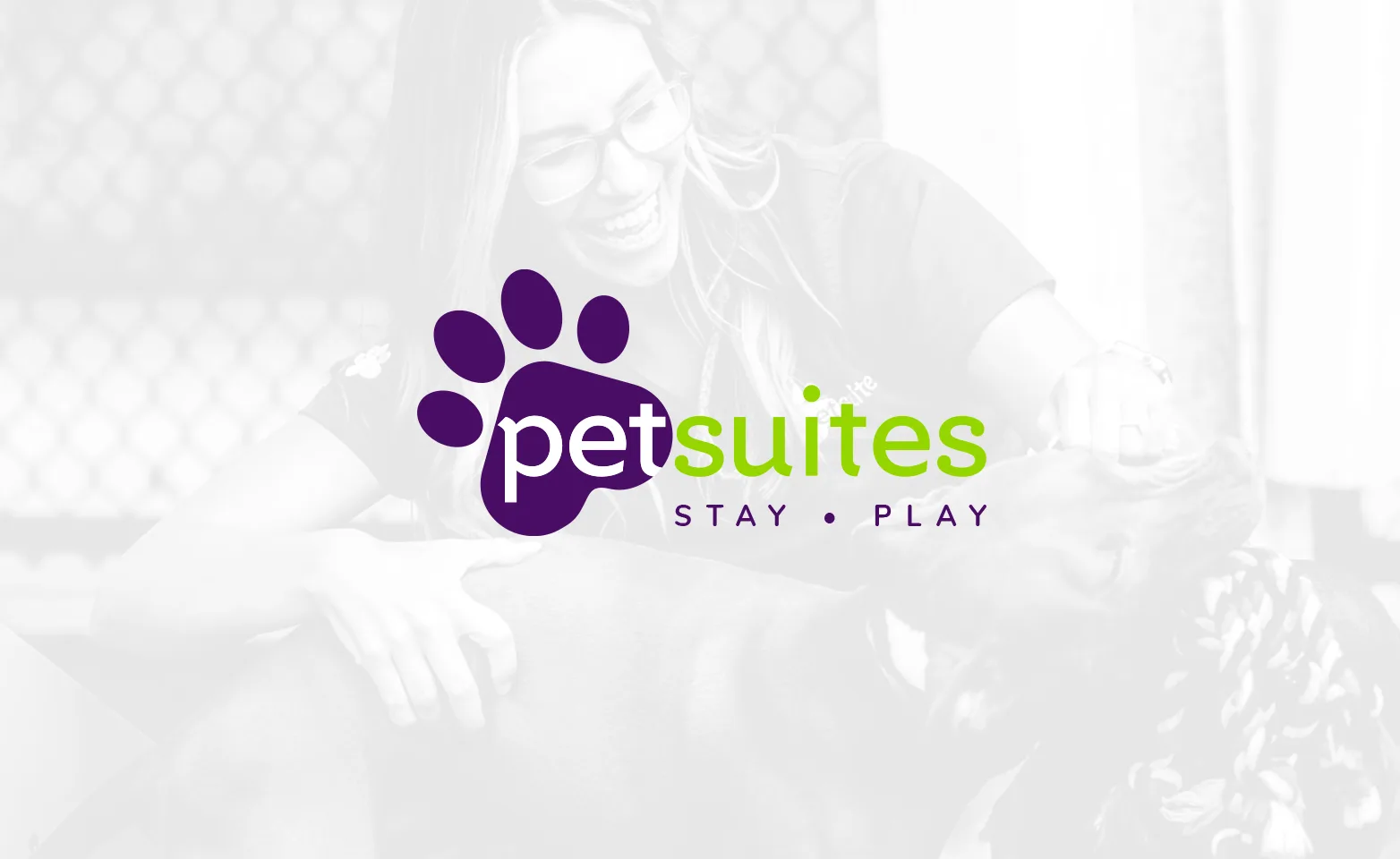 Background photograph of PetSuites animal care specialist smiling and playing with a dog in daycare.