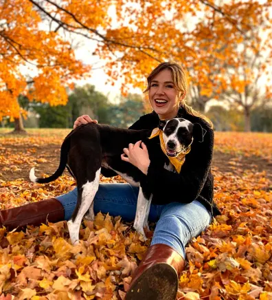Chloe, trainer at The Pet Ranch, sitting in a pile of leaves with black and white dog