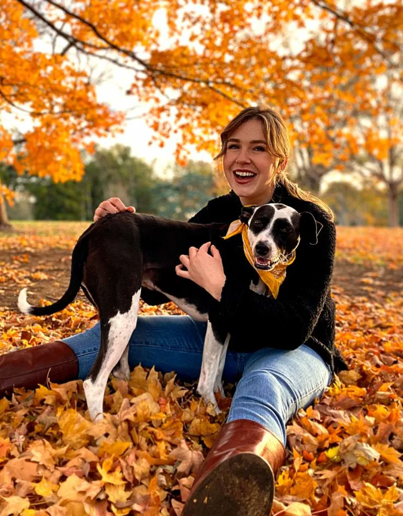 Chloe, trainer at The Pet Ranch, sitting in a pile of leaves with black and white dog