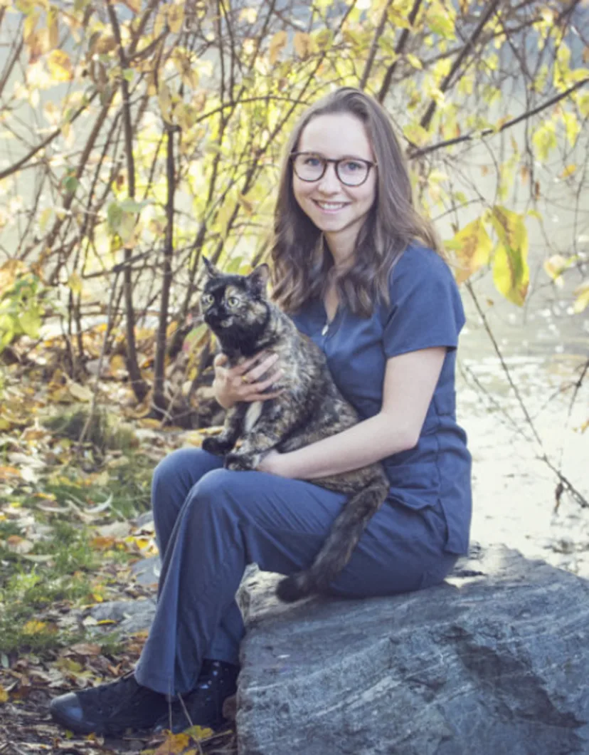 Natalie sitting on a rock and holding a brindle cat