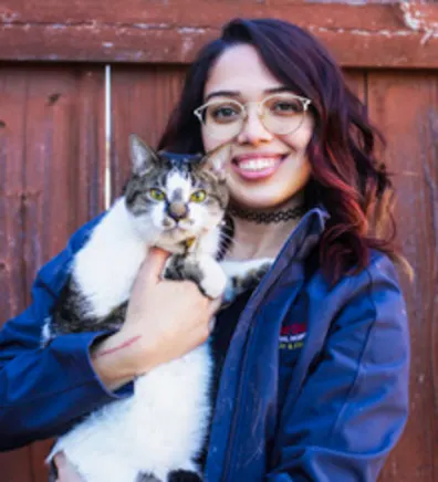 Mercy standing in front of a wood fence holding a white and brown cat Mercy standing in front of a wood fence holding a white and brown cat