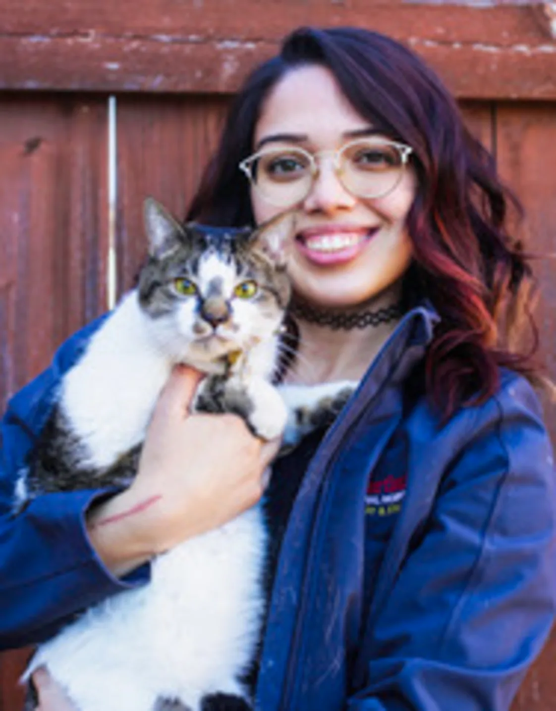Mercy standing in front of a wood fence holding a white and brown cat Mercy standing in front of a wood fence holding a white and brown cat