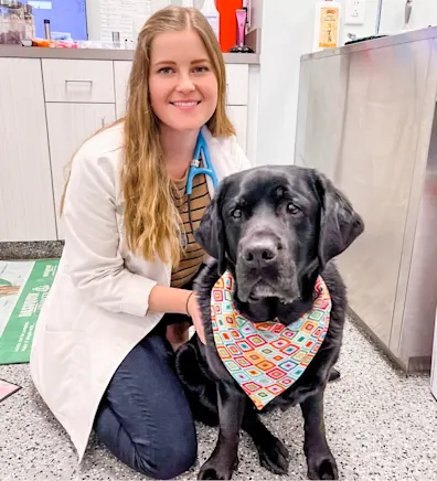 Dr. Elise Mauer smiling kneeling down next to a black dog wearing a bandana Dr. Elise Mauer smiling kneeling down next to a black dog wearing a bandana