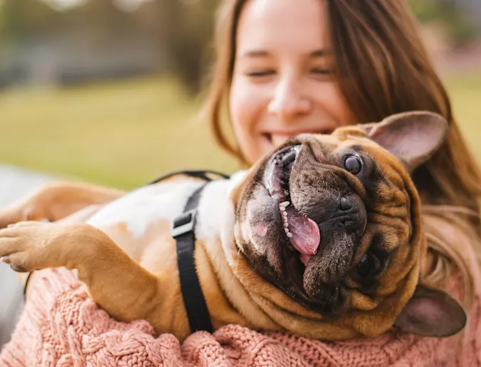 Women holding dog over shoulders as the dogs tongue is out