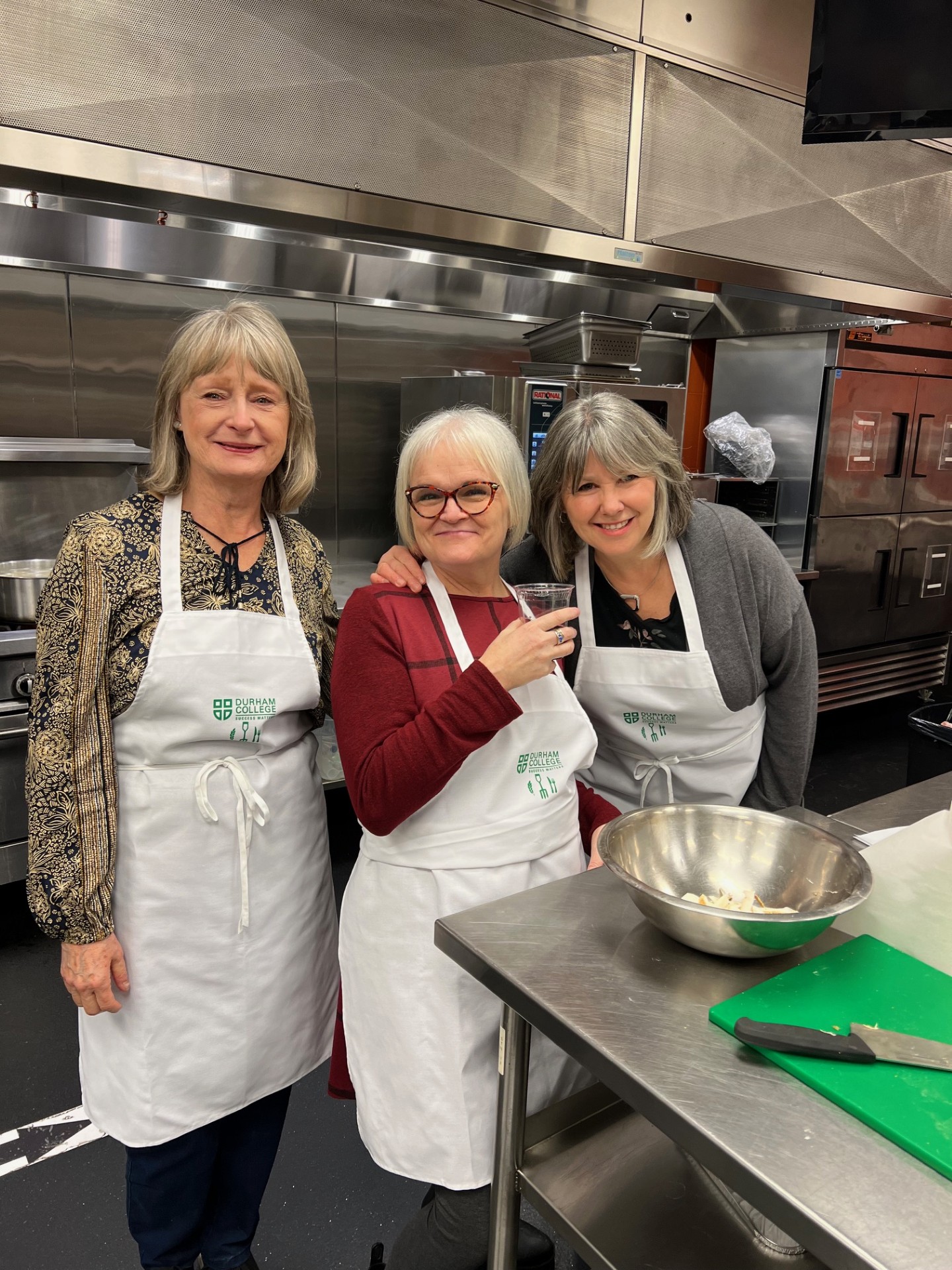 Sandra McBride smiling in a kitchen cooking with two friends.