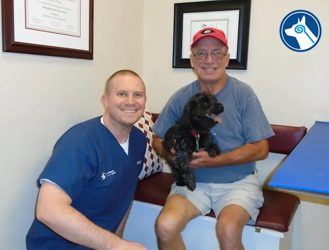 A staff member sitting next to a man who is holding a black poodle mix A staff member sitting next to a man who is holding a black poodle mix