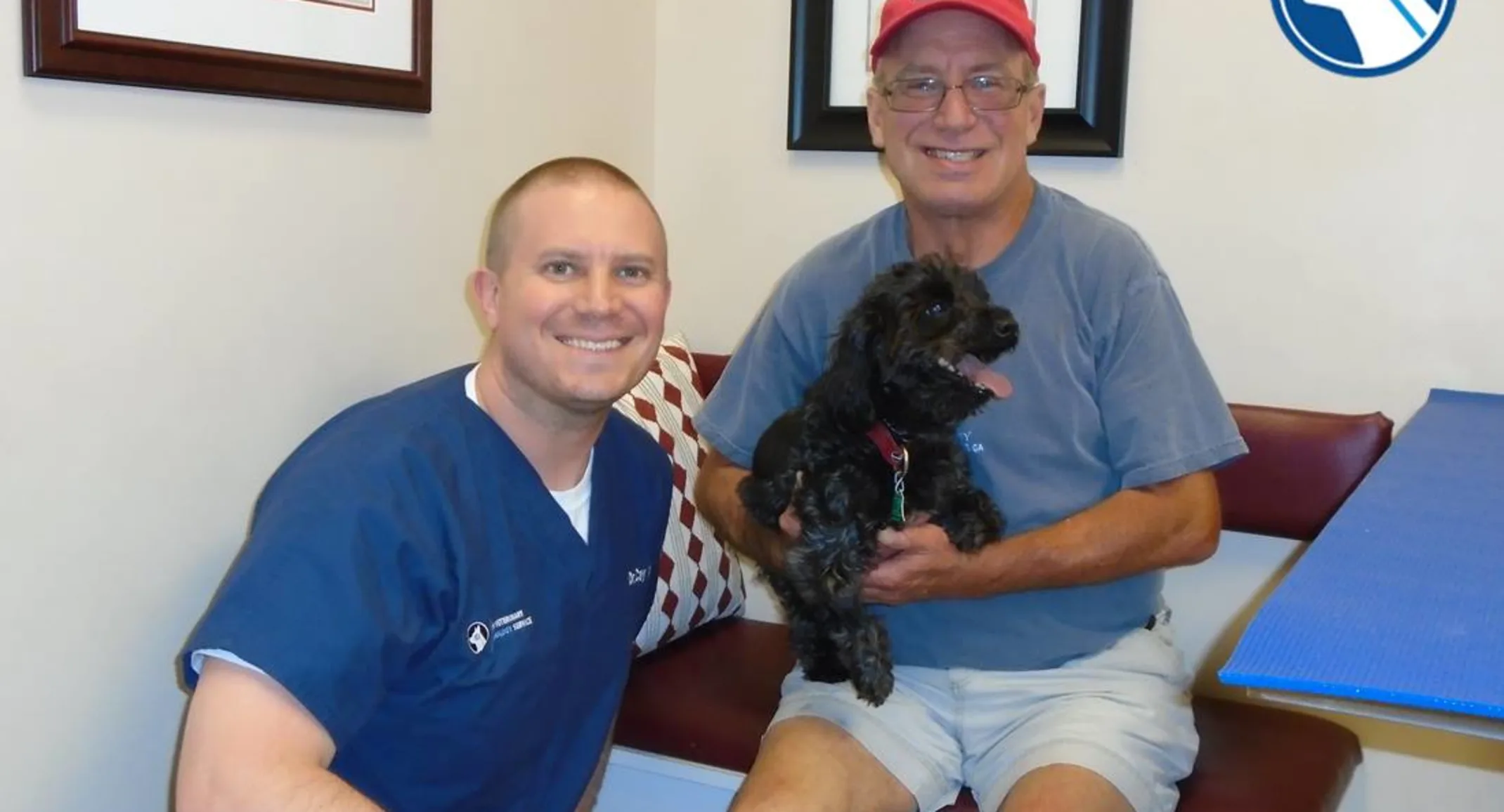 A staff member sitting next to a man who is holding a black poodle mix A staff member sitting next to a man who is holding a black poodle mix