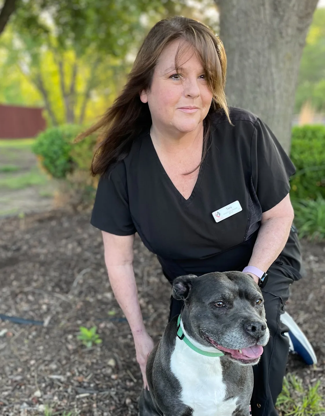 Tara kneeling down in front of a brick wall next to a black dog Tara kneeling down in front of a brick wall next to a black dog