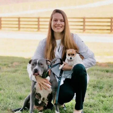 Dr. Kelsea Neitzke posing in a field holding a small dog in her right arm with a large dog to her side