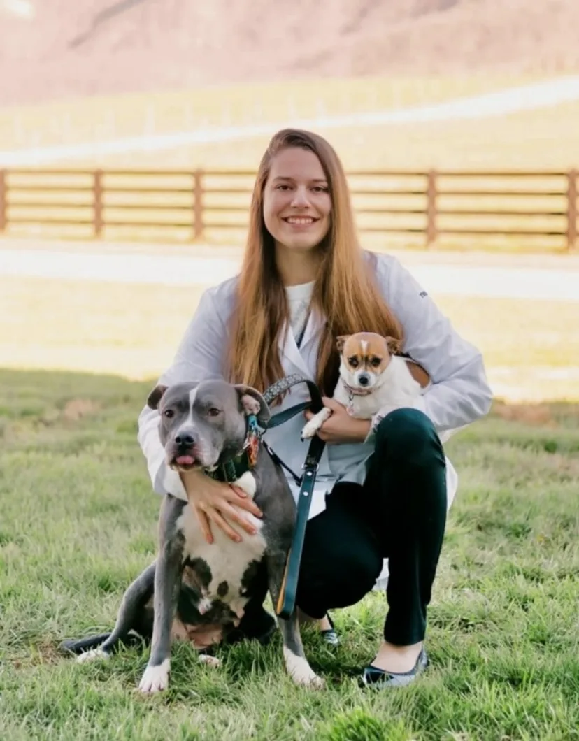 Dr. Kelsea Neitzke posing in a field holding a small dog in her right arm with a large dog to her side