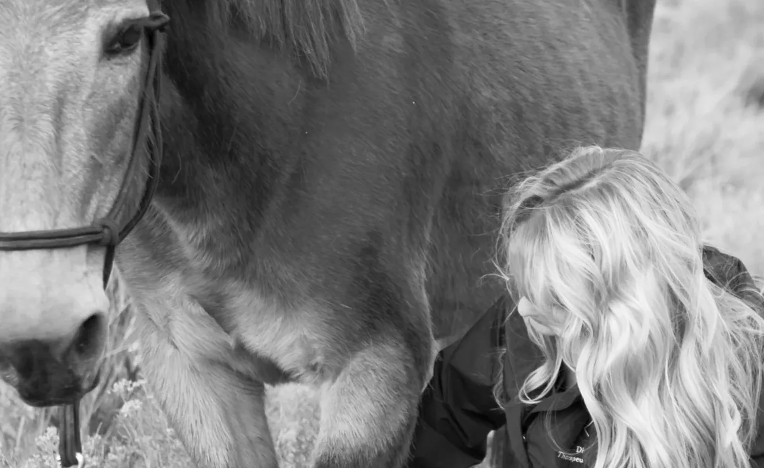 Black and white image of a woman attending a horse.