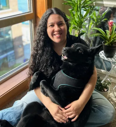 Norma Gomez sitting with a large black dog in her lap in front of a window