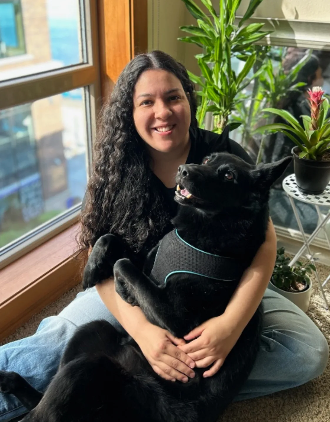 Norma Gomez sitting with a large black dog in her lap in front of a window Norma Gomez sitting with a large black dog in her lap in front of a window