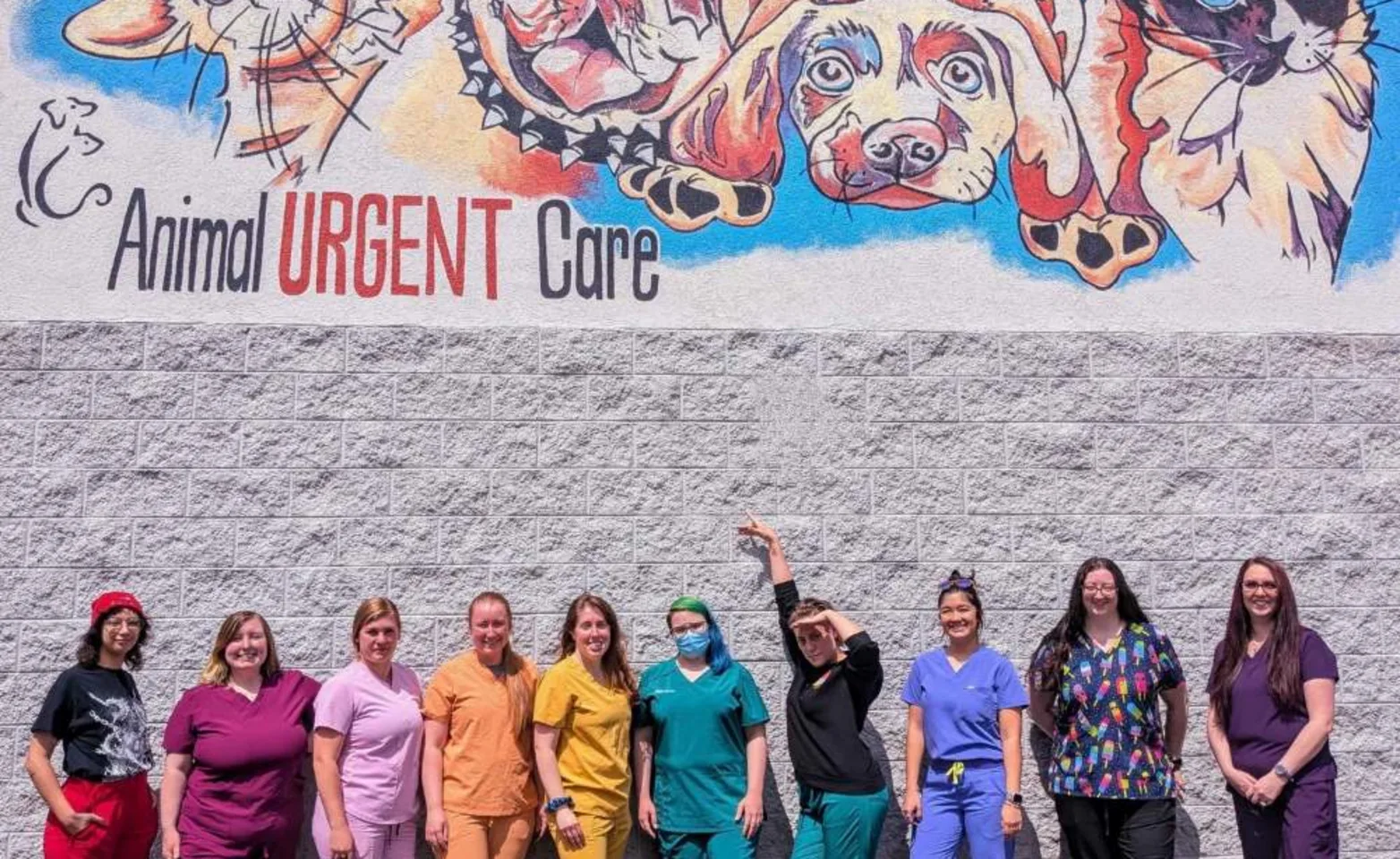 Staff in rainbow colored scrubs standing infront of a mural. Staff in rainbow colored scrubs standing infront of a mural.