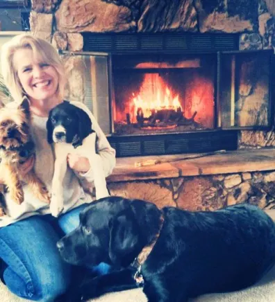 Cristi sitting in front of a fire place with her 3 dogs