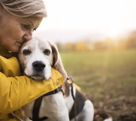 Elder Lady is sitting at a park with her elder dog and she's hugging her dog dearly