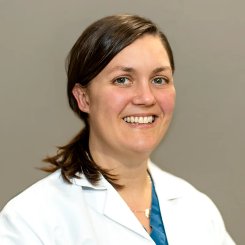 Ruth McDevitt smiling standing in front of a tan wall wearing a white lab coat Ruth McDevitt smiling standing in front of a tan wall wearing a white lab coat
