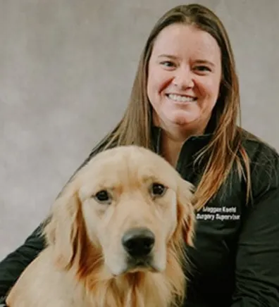 Meggan Koehl smiling in front of a grey backdrop hugging a golden retriever