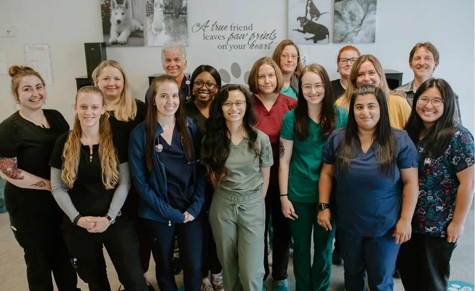 A group of people smiling, standing in a veterinary clinic with animal posters on the wall behind them. A group of people smiling, standing in a veterinary clinic with animal posters on the wall behind them.