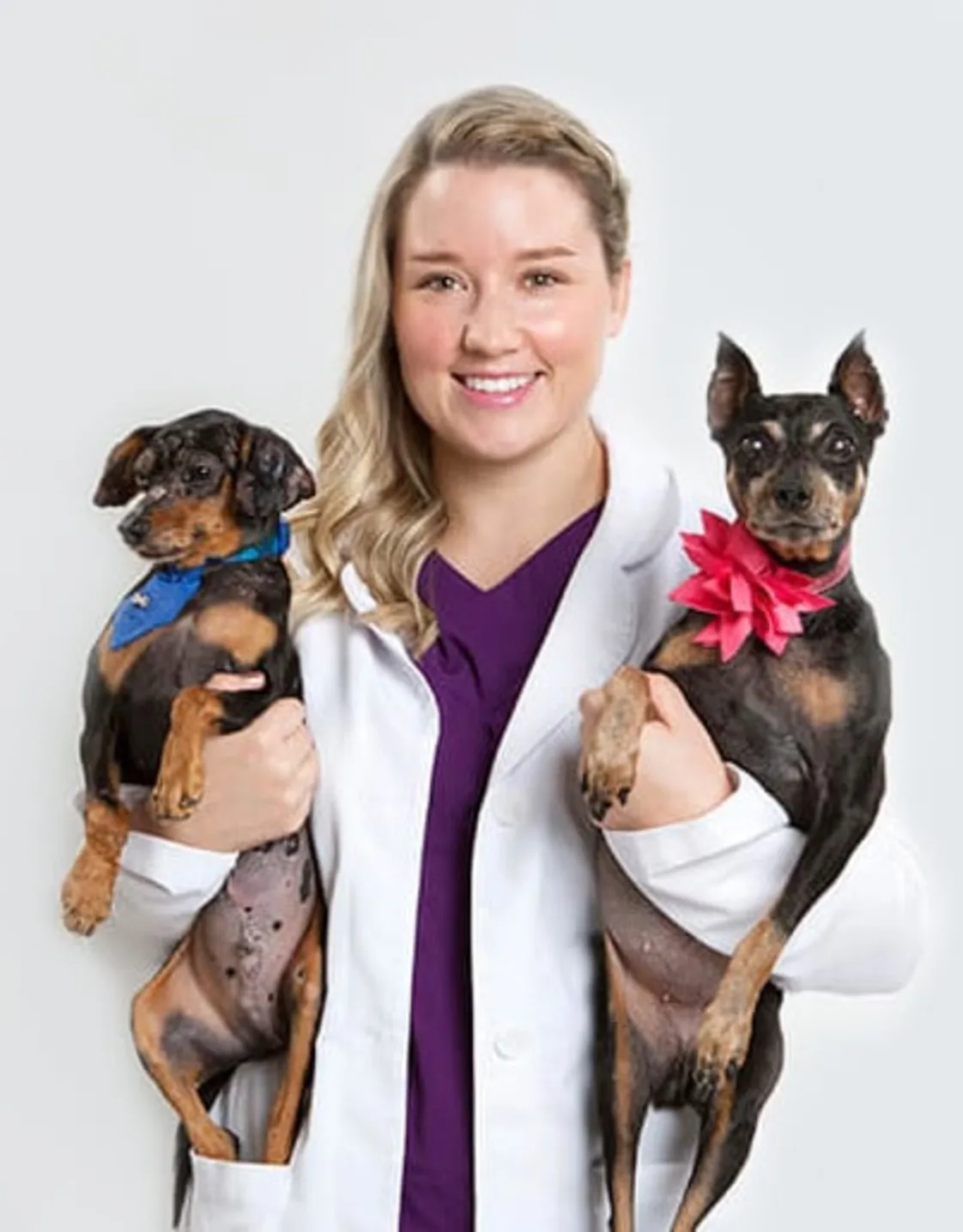 Kathryn McCutcheon holding two black and brown dogs, with the one one her left wearing a blue bandana and the one on the right wearing a pink flower on its neck. Kathryn McCutcheon holding two black and brown dogs, with the one one her left wearing a blue bandana and the one on the right wearing a pink flower on its neck.