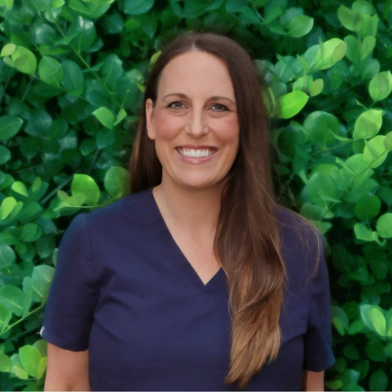 Dr. Beth Lechner sitting down on a grass holding a black dog Dr. Beth Lechner sitting down on a grass holding a black dog