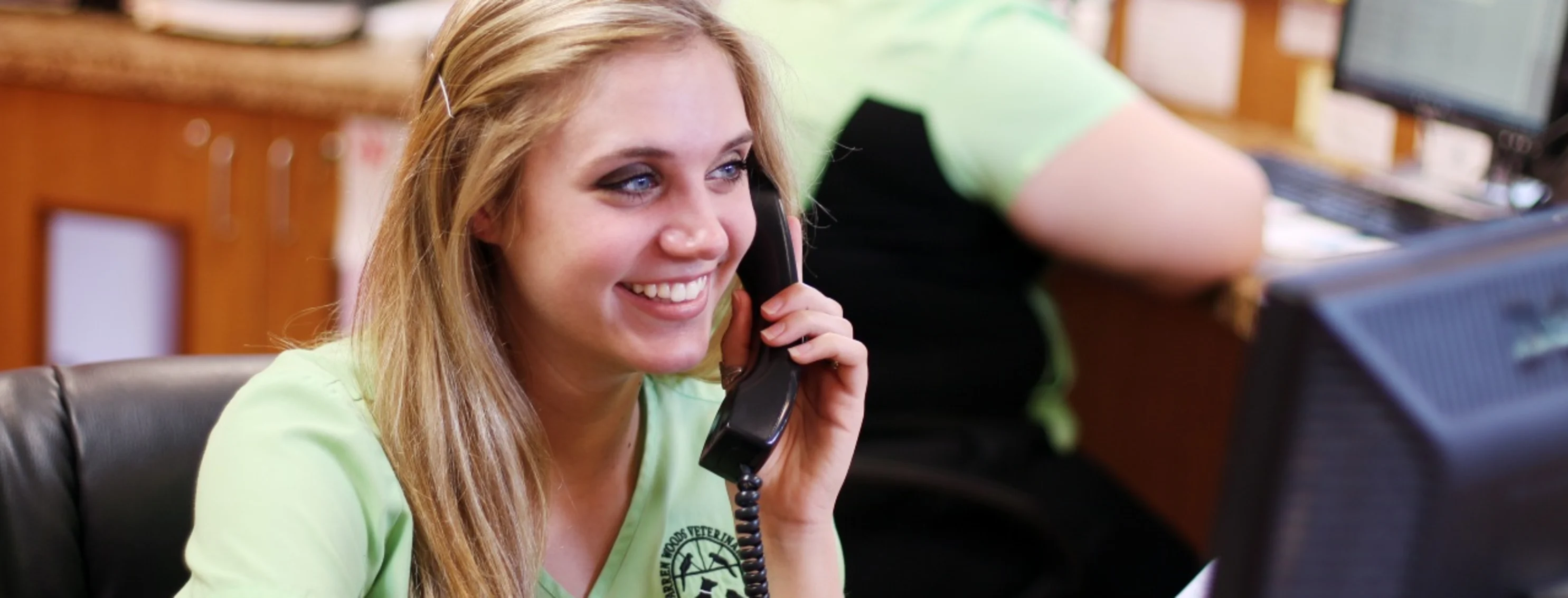 Blonde employee in green shirt smiling while on the phone