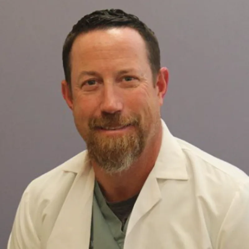 Carl F. Agnello smiling in front of a grey wall wearing a white lab coat Carl F. Agnello smiling in front of a grey wall wearing a white lab coat