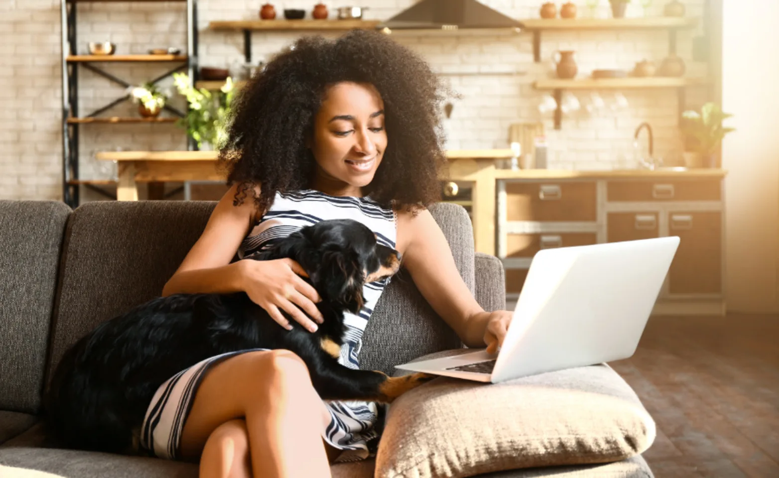 Woman using her laptop with her dog on the couch at home