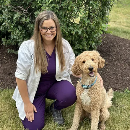 Dr. Nicole Bell kneeling next to a goldendoodle outside