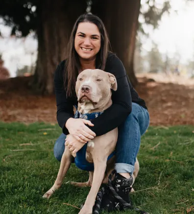 Patricia OJala kneeling and wrapping her arms around a Pitbull dog
