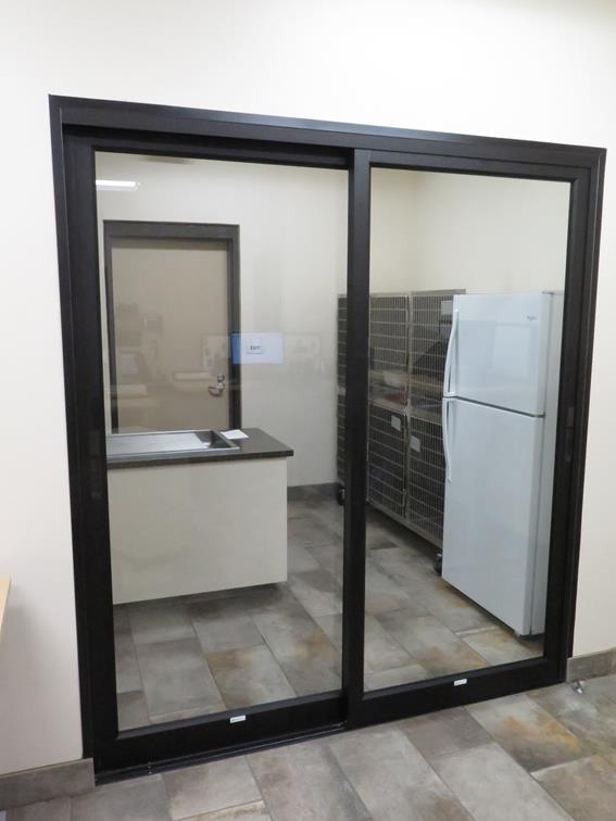 An exam room with table, kennels, and a fridge behind a glass door.