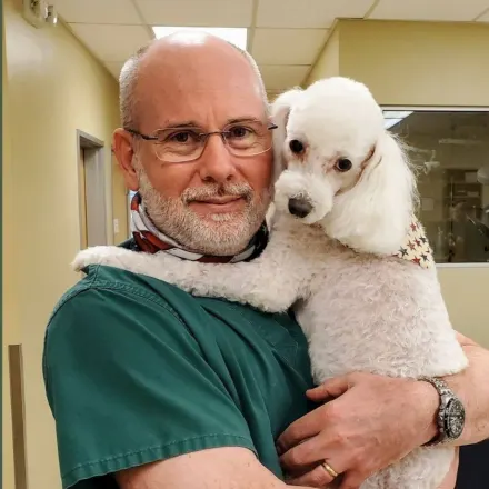 Steven Hibler smiling inside holding a small white poodle.