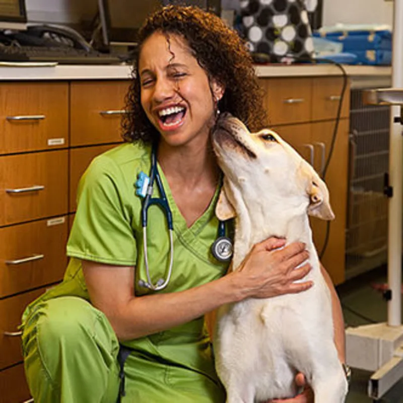 Dr. Adina Mosby kneeling inside while hugging a dog Dr. Adina Mosby kneeling inside while hugging a dog