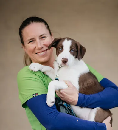 Dr. Lucy Shoemaker holding a brown and white puppy with green and blue scrubs on