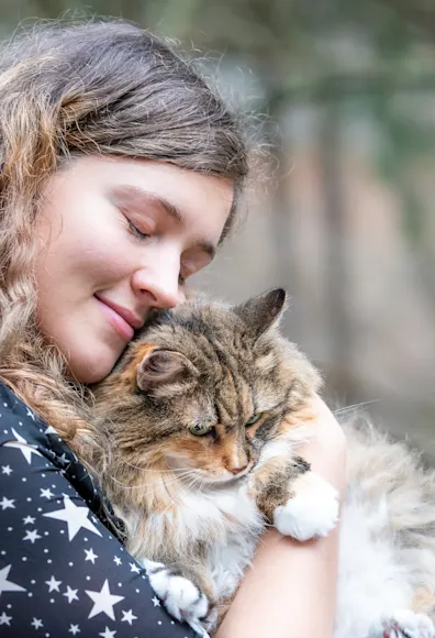 Woman lovingly hugging her fluffy cat outside in a park. Woman lovingly hugging her fluffy cat outside in a park.