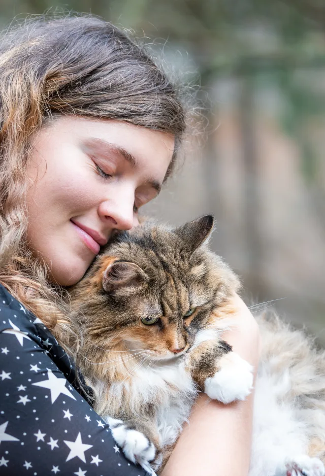 Woman lovingly hugging her fluffy cat outside in a park. 
