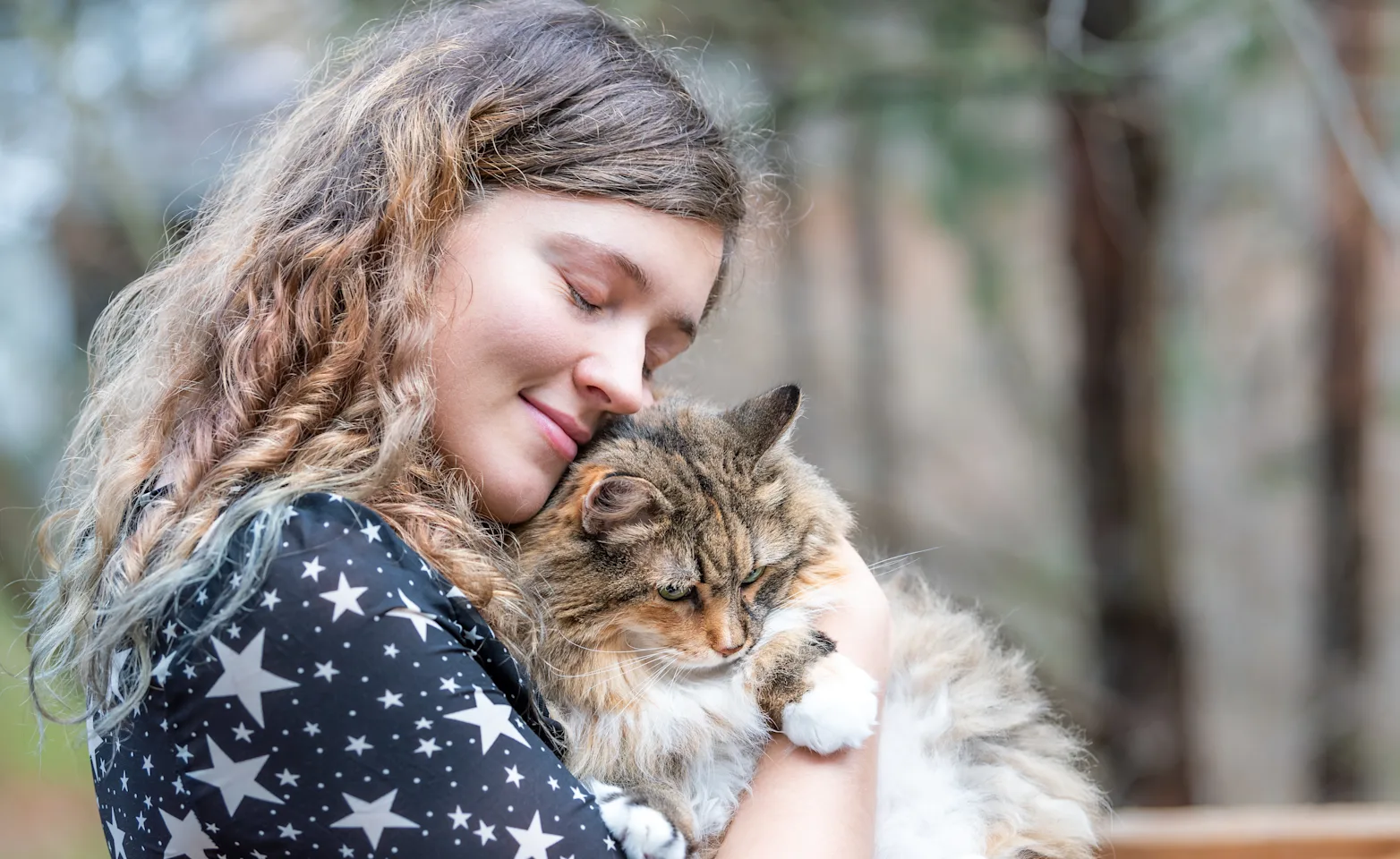 Woman lovingly hugging her fluffy cat outside in a park. Woman lovingly hugging her fluffy cat outside in a park.