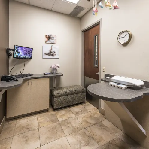 Hillside Animal Hospital Exam Room 4 shows a small scale on placed on a desk to weigh your smaller animals on.  There's a half sized cushioned bench and a doctor's desk to check you in. 