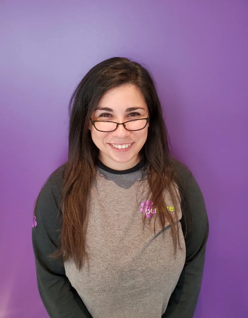 Image of friendly person wearing glasses smiling at the camera with a purple background.
