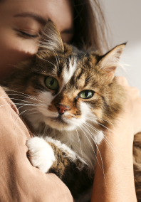 Lady embracing and kissing her Calico Cat in her arms.