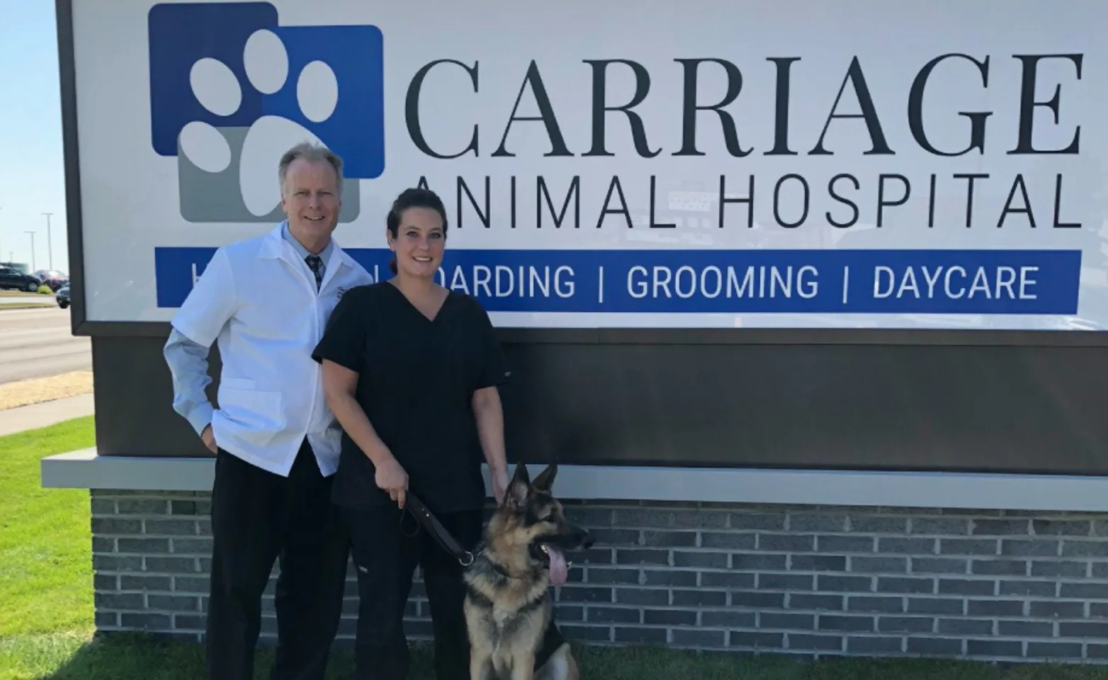 Front sign and Dr. Jeremy Buishas with staff member and german shepherd at Carriage Animal Hospital