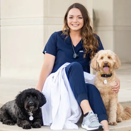 Dr. Landri Prado sitting outside on building steps with two dogs