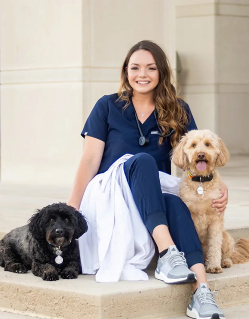 Dr. Landri Prado sitting outside on building steps with two dogs