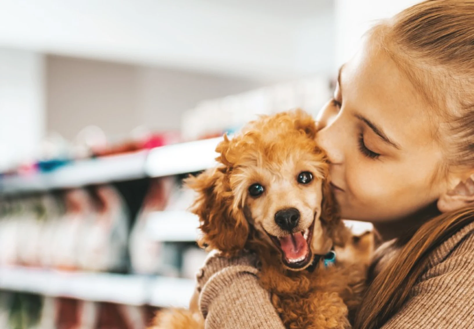 Girl holding and kissing a small dog while in a store