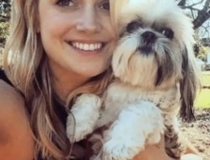 a woman smiles while holding a small dog a woman smiles while holding a small dog