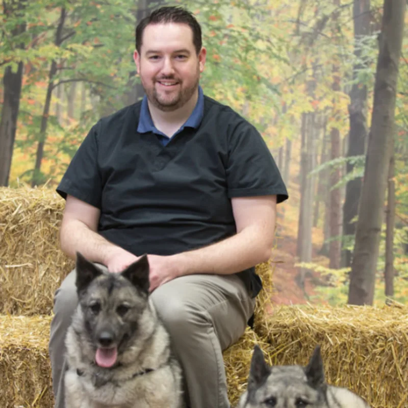 Dr. Jeff Brisebois sitting on hay with two dogs Dr. Jeff Brisebois sitting on hay with two dogs