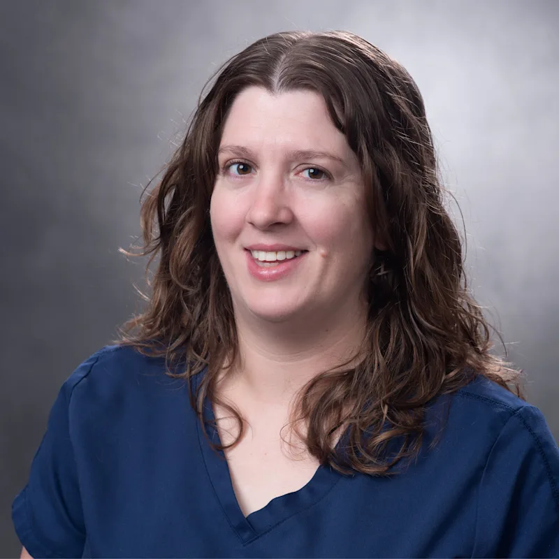 White woman with long brown curly hair in blue shirt holding white and grey cat. White woman with long brown curly hair in blue shirt holding white and grey cat.
