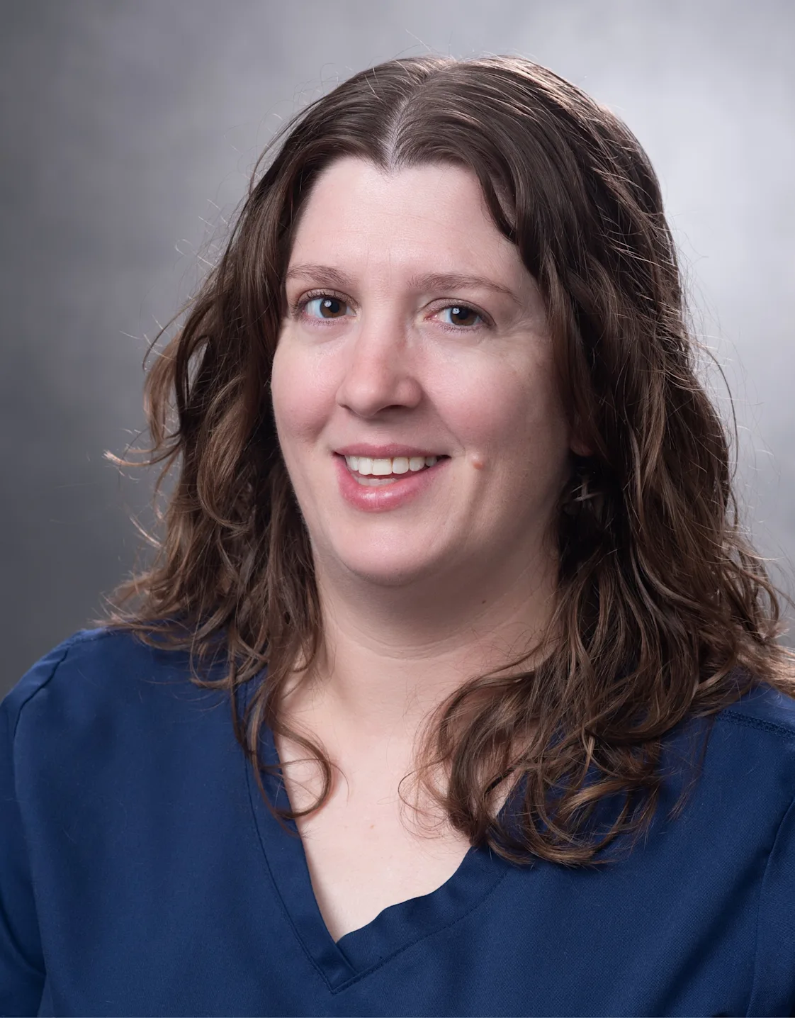 White woman with long brown curly hair in blue shirt holding white and grey cat. White woman with long brown curly hair in blue shirt holding white and grey cat.