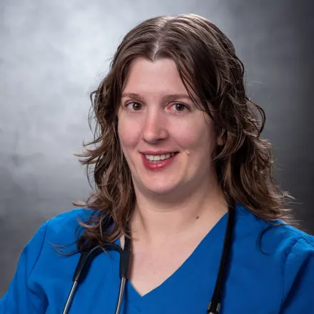 White woman with long brown curly hair in blue shirt holding white and grey cat.